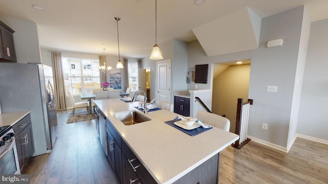 kitchen with sink, stainless steel appliances, an inviting chandelier, light hardwood / wood-style floors, and a kitchen island with sink