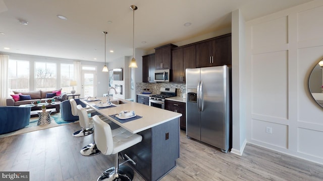 kitchen featuring sink, light hardwood / wood-style flooring, an island with sink, dark brown cabinetry, and stainless steel appliances