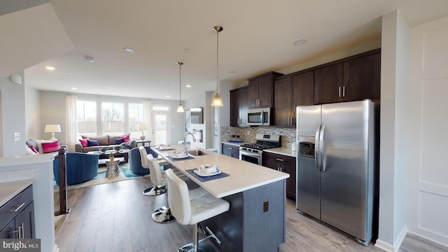 kitchen with appliances with stainless steel finishes, light wood-type flooring, a kitchen breakfast bar, sink, and a center island with sink