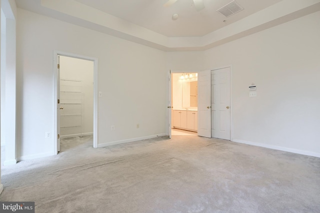 unfurnished bedroom featuring light carpet, a walk in closet, a tray ceiling, ceiling fan, and a closet