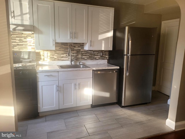 kitchen with backsplash, sink, light stone counters, white cabinetry, and stainless steel appliances