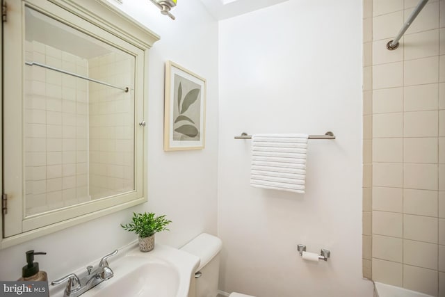 bathroom featuring tiled shower, sink, and toilet