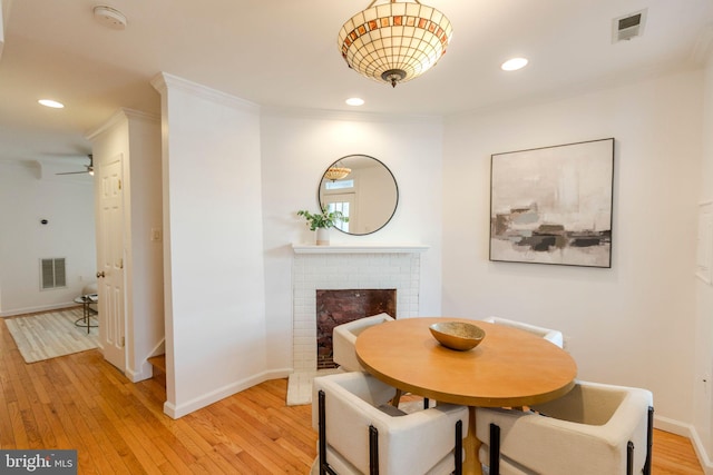 dining space featuring a fireplace, light wood-type flooring, ceiling fan, and crown molding