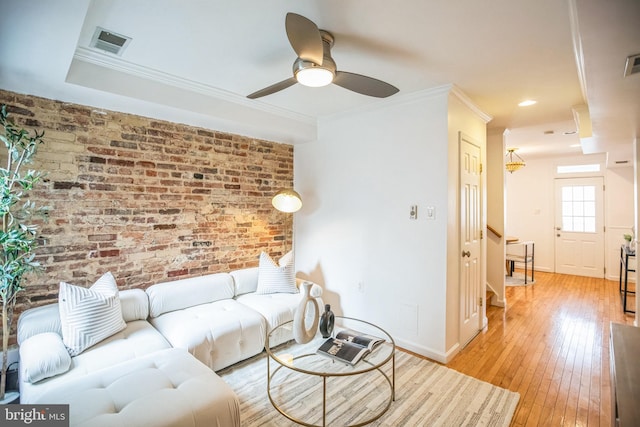 living room featuring ceiling fan, light hardwood / wood-style floors, ornamental molding, and brick wall