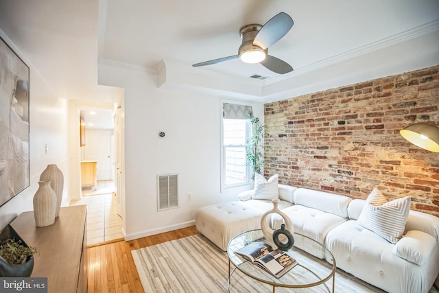 living room featuring ceiling fan, crown molding, brick wall, and light hardwood / wood-style flooring