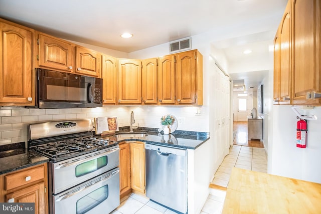 kitchen with dark stone counters, sink, decorative backsplash, appliances with stainless steel finishes, and light tile patterned flooring