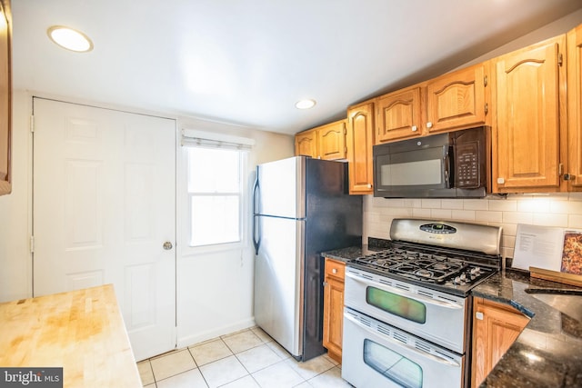 kitchen featuring gas stove, tasteful backsplash, dark stone countertops, stainless steel fridge, and light tile patterned floors