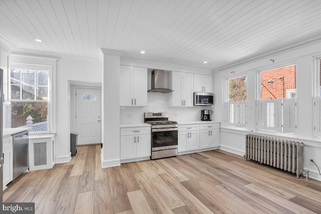 kitchen featuring white cabinetry, radiator heating unit, wall chimney exhaust hood, stainless steel appliances, and light wood-type flooring