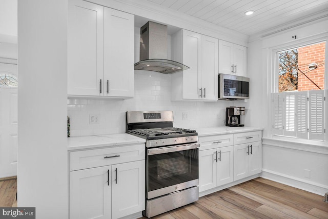 kitchen with white cabinets, wall chimney exhaust hood, light hardwood / wood-style floors, and stainless steel appliances