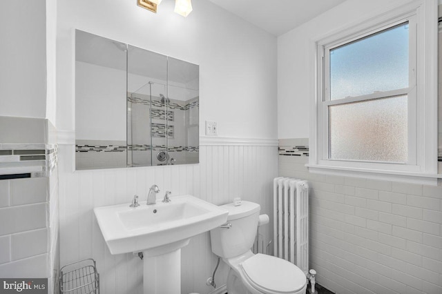 bathroom featuring radiator, sink, tile walls, and toilet