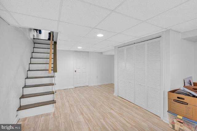 basement featuring a paneled ceiling and light hardwood / wood-style flooring