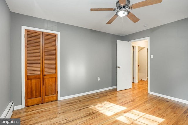 unfurnished bedroom with light hardwood / wood-style floors, a closet, a baseboard heating unit, and ceiling fan