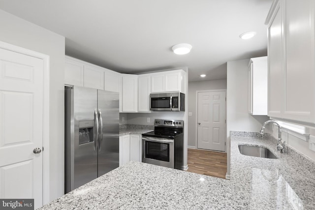 kitchen featuring white cabinets, appliances with stainless steel finishes, light stone counters, and sink