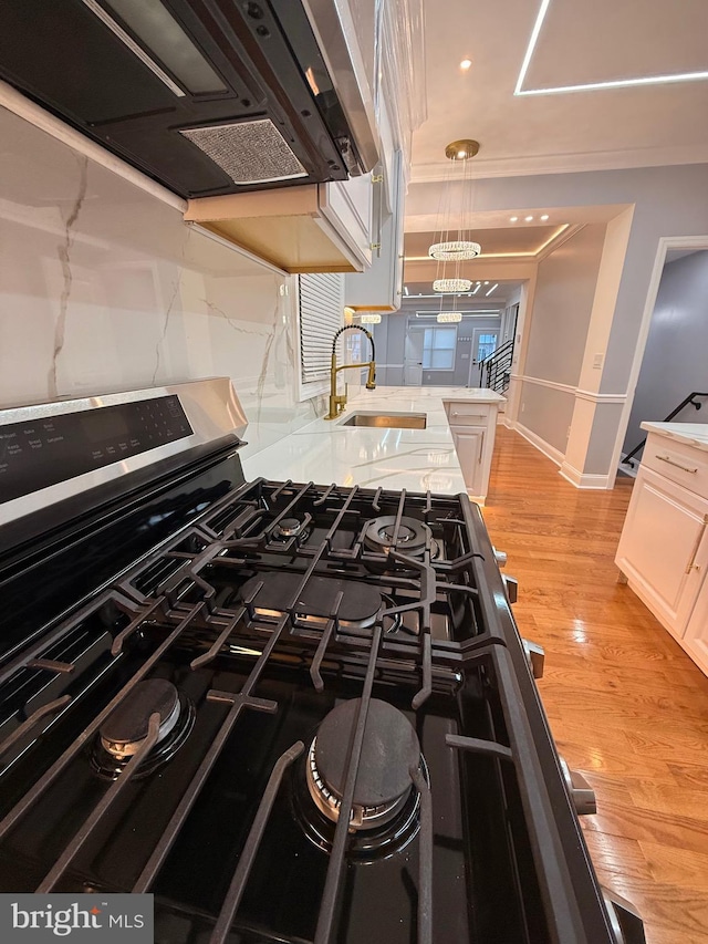 kitchen with gas stove, sink, extractor fan, light hardwood / wood-style floors, and decorative light fixtures