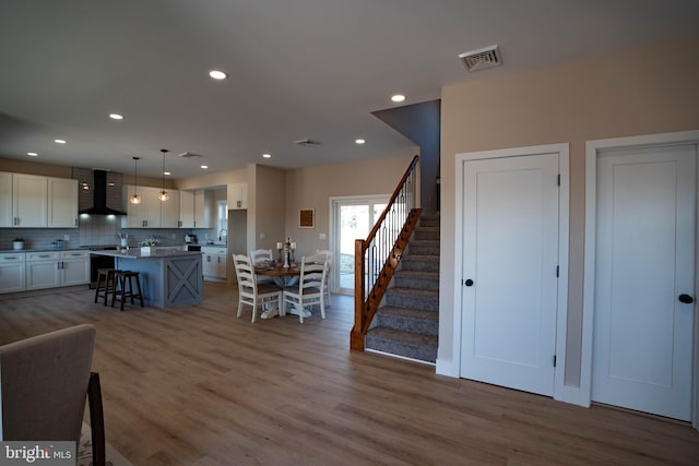 interior space with a kitchen bar, wall chimney range hood, decorative light fixtures, white cabinets, and a center island