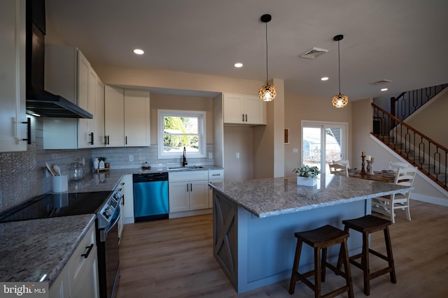 kitchen with wall chimney range hood, sink, light hardwood / wood-style flooring, white cabinetry, and stainless steel appliances