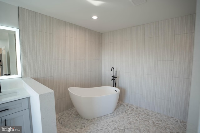 bathroom with a tub to relax in, tile patterned flooring, vanity, and tile walls