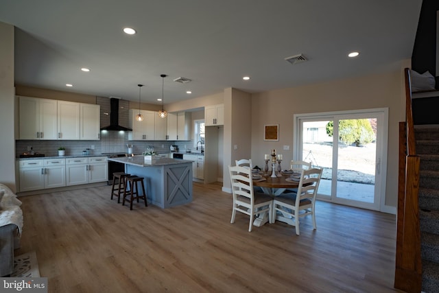 kitchen featuring a kitchen island, wall chimney range hood, decorative light fixtures, light hardwood / wood-style floors, and white cabinetry