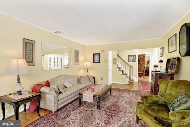 living room featuring visible vents, ornamental molding, light wood-type flooring, baseboards, and stairs