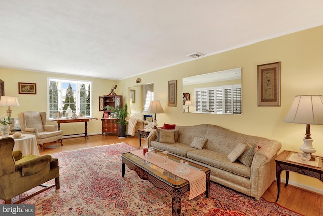 living room with baseboards, ornamental molding, visible vents, and light wood-style floors