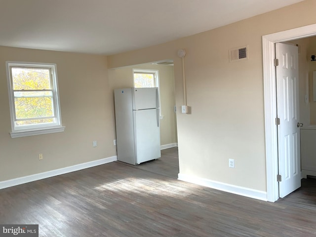 unfurnished bedroom with dark hardwood / wood-style flooring, white refrigerator, and multiple windows