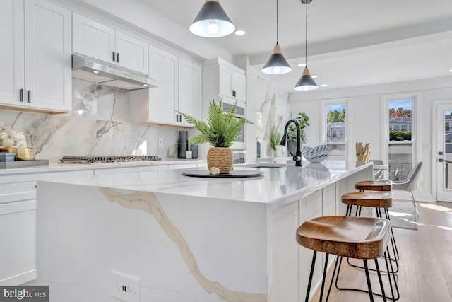 kitchen with light hardwood / wood-style flooring, a large island with sink, decorative light fixtures, stainless steel gas stovetop, and white cabinets