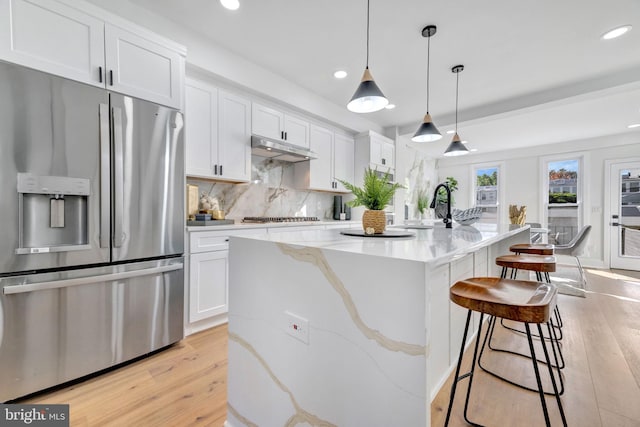 kitchen featuring white cabinets, light wood-type flooring, stainless steel appliances, and light stone countertops