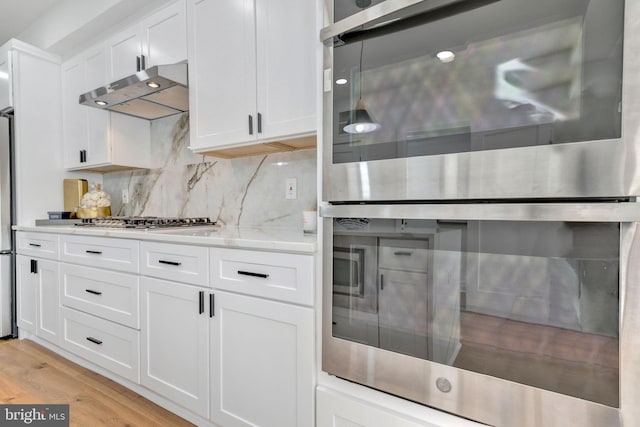 kitchen featuring white cabinetry, stainless steel appliances, light stone counters, backsplash, and light hardwood / wood-style floors