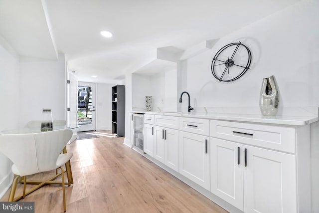 bar with white cabinets, sink, light hardwood / wood-style floors, light stone counters, and beverage cooler