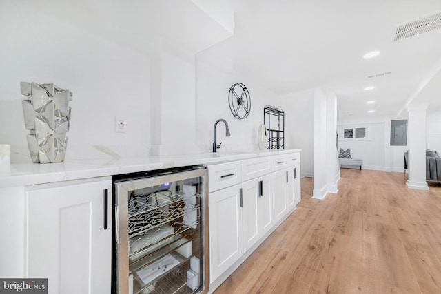 bar featuring sink, light hardwood / wood-style flooring, light stone countertops, white cabinetry, and beverage cooler