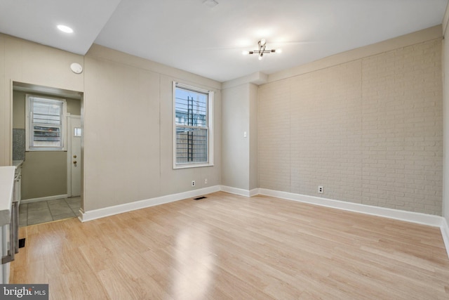 unfurnished room featuring brick wall, a notable chandelier, and light wood-type flooring