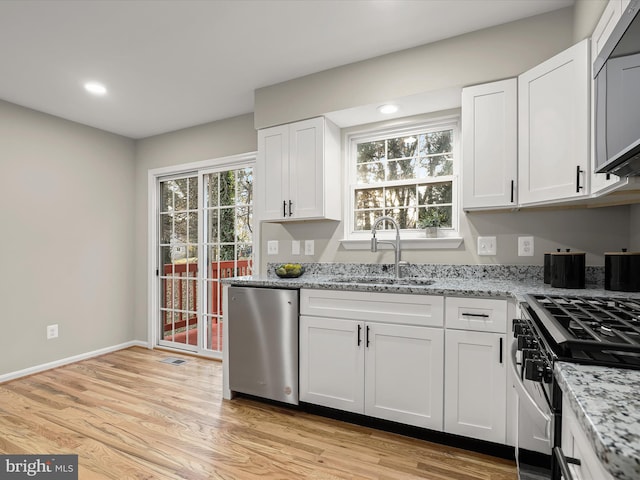 kitchen with light stone countertops, white cabinetry, sink, stainless steel appliances, and light hardwood / wood-style flooring