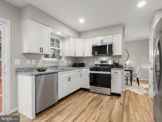 kitchen with white cabinetry, sink, stainless steel appliances, light stone counters, and light hardwood / wood-style flooring