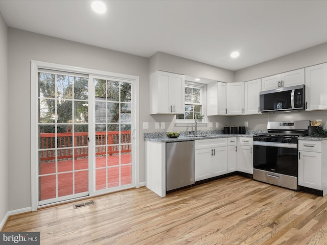 kitchen with appliances with stainless steel finishes, light hardwood / wood-style floors, and white cabinetry