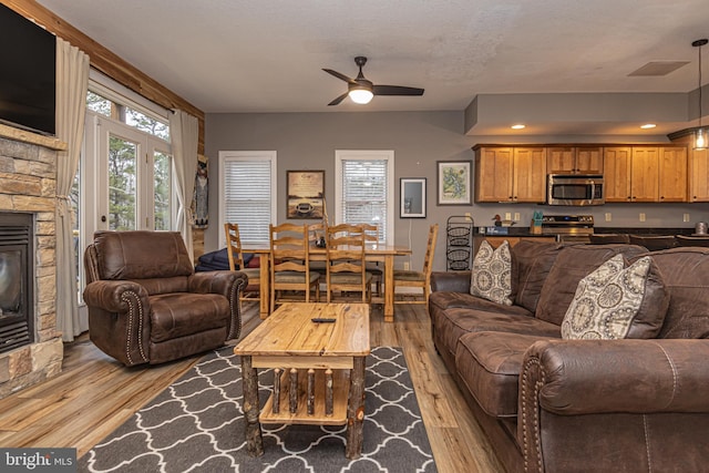 living room featuring ceiling fan, light hardwood / wood-style floors, a stone fireplace, and plenty of natural light