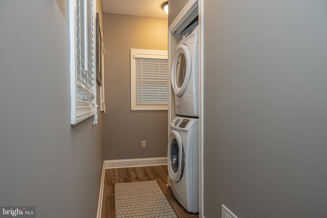 laundry area with a textured ceiling, stacked washer / dryer, and dark wood-type flooring