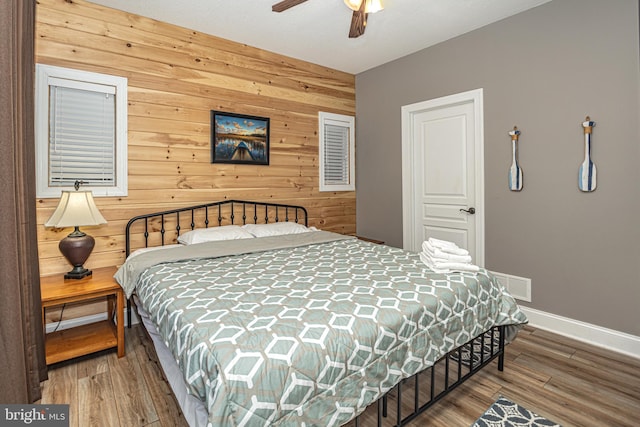 bedroom featuring ceiling fan, wood-type flooring, and wooden walls