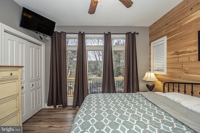 bedroom with hardwood / wood-style floors, wood walls, ceiling fan, a textured ceiling, and a closet