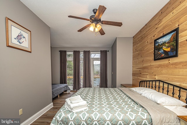 bedroom featuring access to exterior, a textured ceiling, ceiling fan, wooden walls, and dark hardwood / wood-style floors