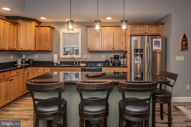 kitchen with a breakfast bar, sink, stainless steel refrigerator with ice dispenser, decorative light fixtures, and a kitchen island