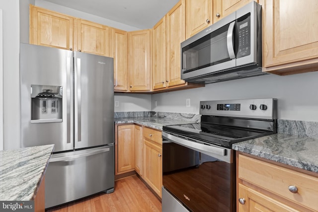 kitchen with light stone countertops, appliances with stainless steel finishes, light hardwood / wood-style floors, and light brown cabinetry