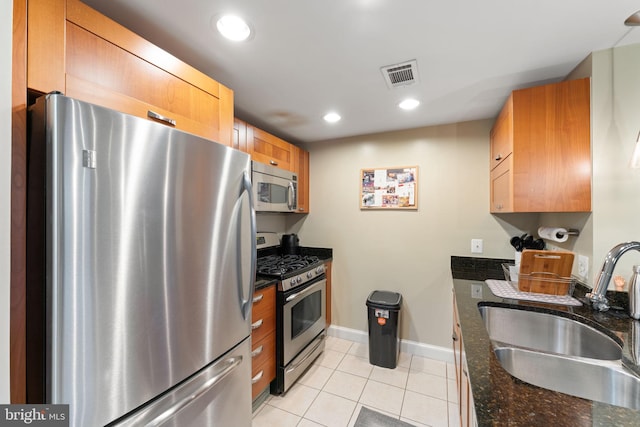 kitchen with dark stone countertops, light tile patterned flooring, sink, and stainless steel appliances