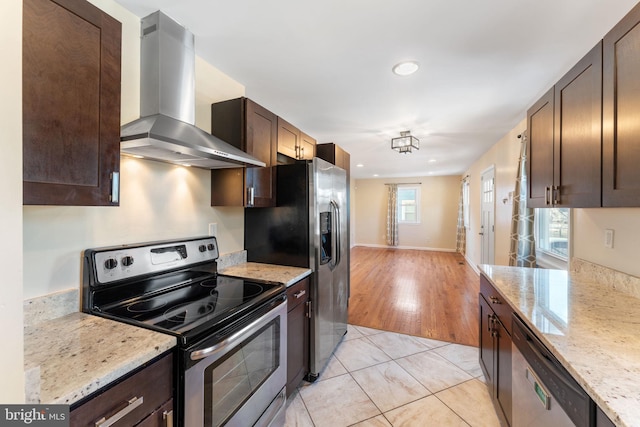 kitchen with wall chimney range hood, light tile patterned flooring, stainless steel appliances, dark brown cabinets, and light stone counters