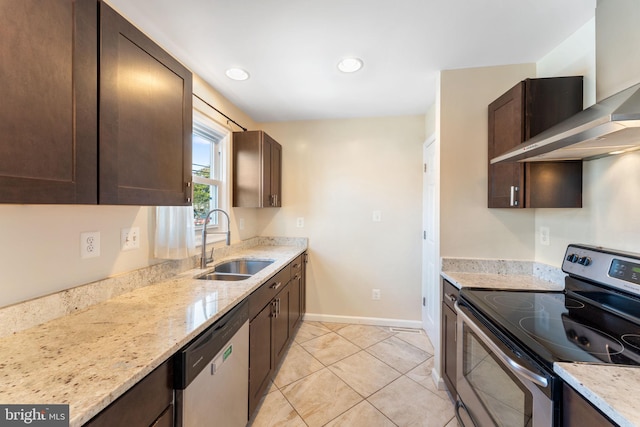 kitchen featuring dark brown cabinetry, appliances with stainless steel finishes, wall chimney exhaust hood, sink, and light stone counters