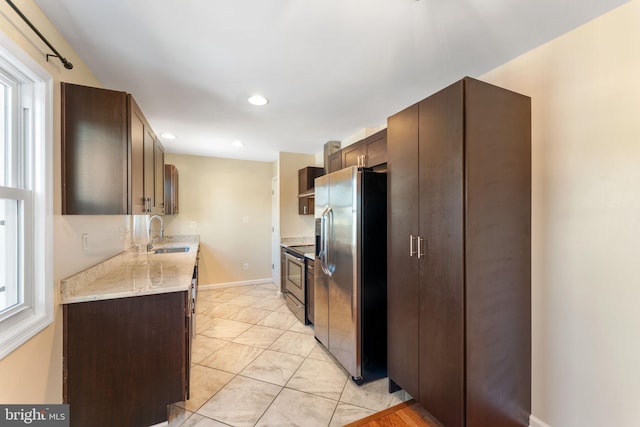 kitchen featuring dark brown cabinetry, appliances with stainless steel finishes, wall chimney exhaust hood, sink, and light stone counters