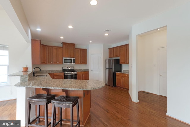 kitchen featuring sink, appliances with stainless steel finishes, hardwood / wood-style floors, a kitchen breakfast bar, and kitchen peninsula