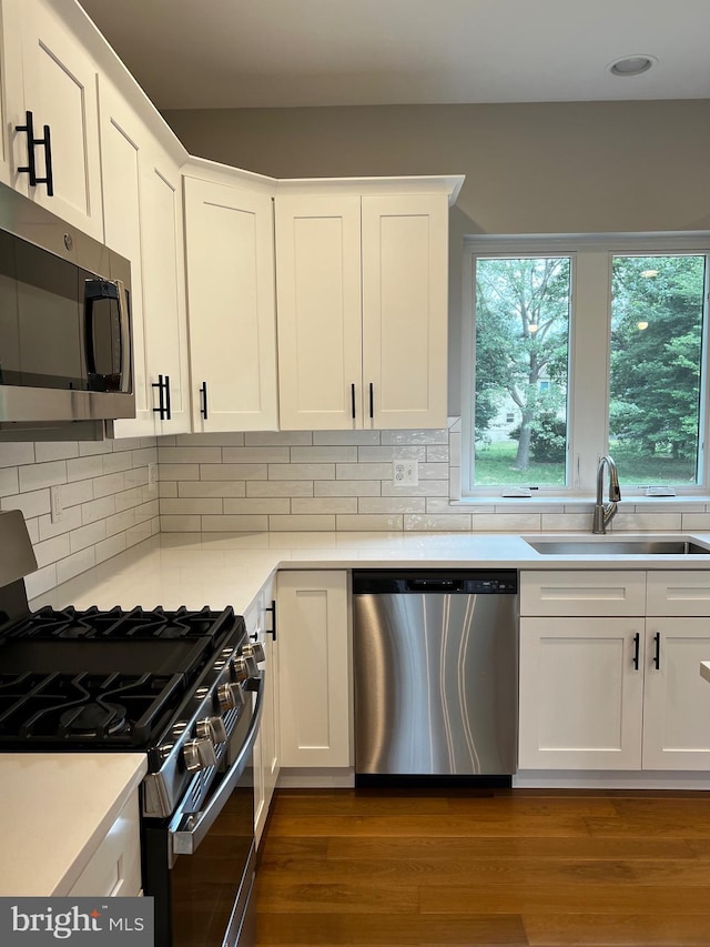 kitchen with appliances with stainless steel finishes, white cabinetry, dark wood-type flooring, and sink