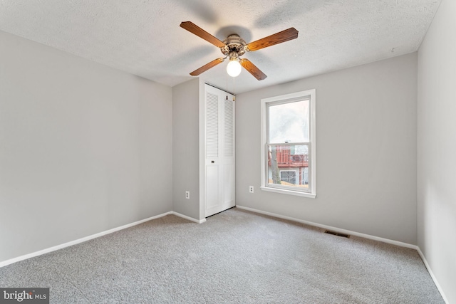 unfurnished bedroom with a textured ceiling, ceiling fan, light carpet, and a closet