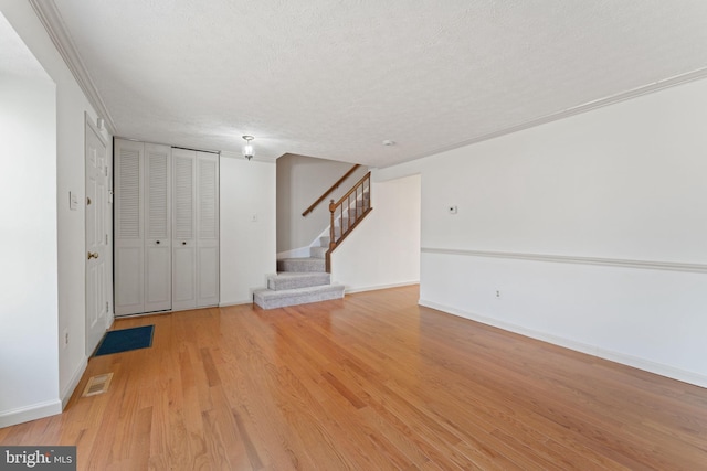 interior space featuring light wood-type flooring, a textured ceiling, and ornamental molding