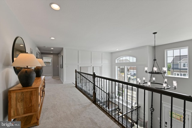 hall featuring light colored carpet and an inviting chandelier